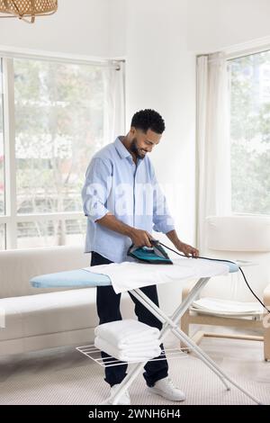 Happy young African homeowner man ironing white towels Stock Photo