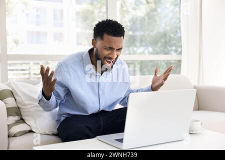 Angry concerned young African business man shouting at laptop Stock Photo