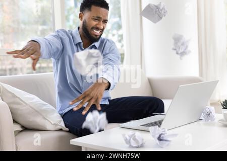 Worried nervous African freelance employee man throwing crumpled documents Stock Photo