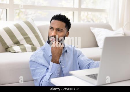 Serious thoughtful young African freelance business man working at laptop Stock Photo