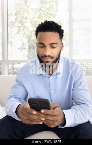 Serious young handsome Black man typing on mobile phone Stock Photo
