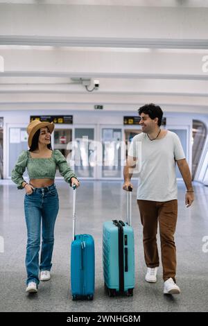 vertical portrait Latin multicultural traveler couple arriving at the airport terminal with their luggage Stock Photo