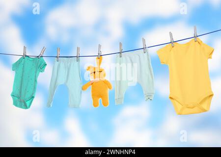 Baby clothes and crochet toy drying on washing line against sky Stock Photo