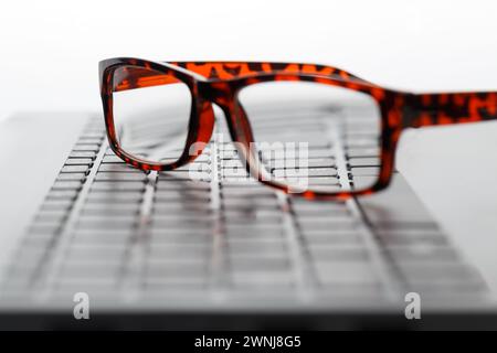 Glasses with black and red frames lie on the keyboard of the laptop. Stock Photo