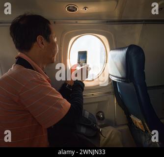 Passenger taking photos using his smartphone through the aircraft window.  Plane taking off with a running propeller. Alaska. Stock Photo