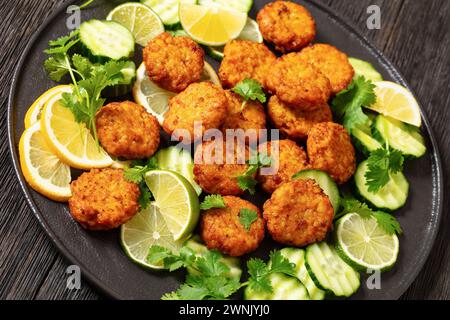 fried rice patties, rice tikki, indian style on black plate served with cucumber, lemon, lime slices and cilantro, close-up Stock Photo