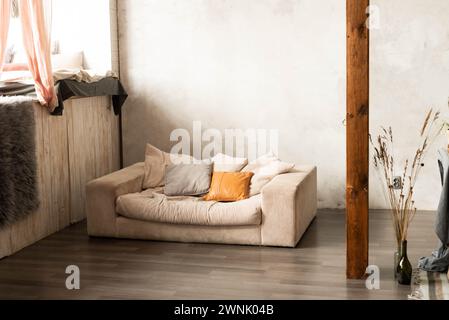 Home interior with gray sofa and pillows, vase with decorative flowers, wooden prop, blank wall and bed near window with pink curtains and another tex Stock Photo