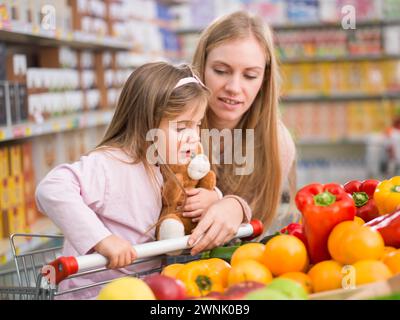 Mother and daughter doing grocery shopping together, they are choosing fruits and vegetables in the produce section Stock Photo