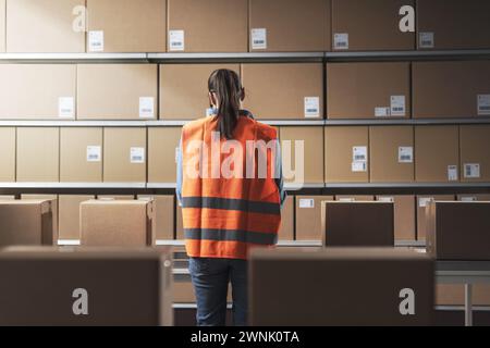 Female warehouse worker checking boxes on the conveyor belt, back view Stock Photo