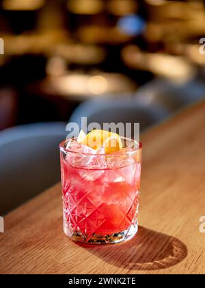 Transparent pink alcohol cocktail with ice, aperol and gin on bar counter in restaurant interior. Alcohol cocktail decorated orange zest spiral. Cold alcoholic cocktail in bar or nightclub. Copy space Stock Photo