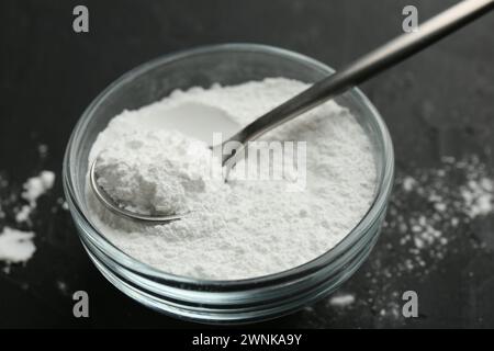 Baking powder in bowl and spoon on black table, closeup Stock Photo