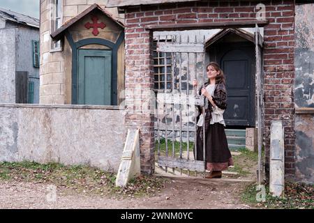 Young woman stands at the gates of a retro medieval church in wild west, America. Vintage clothes on Halloween  style 18-19th century Stock Photo