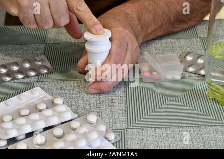 A man, having taken the medicine with his finger, closes the medicine jar. Medicines are on the table. Stock Photo