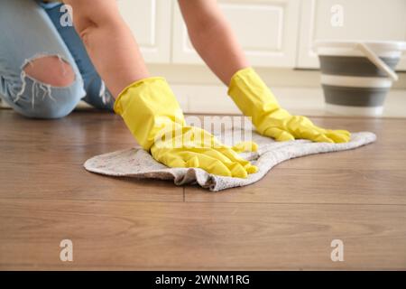 A woman washes the floor with her hands in a home kitchen, manual labor. Women's hands in yellow gloves while cleaning the kitchen Stock Photo