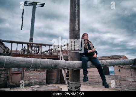 A woman pirate with a dirty face sits on a ship against a stormy sky Stock Photo