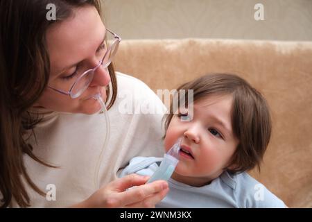 Woman mother using an aspirator to clear snot from baby's nose Stock Photo