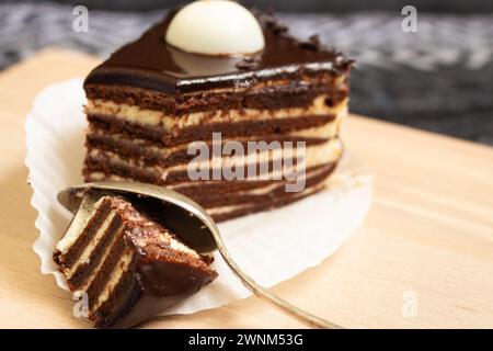 Chocolate layer cake with spoon. Biscuit cake with melted ganache on top. Slice of creamy tart. Vanilla and cocoa layer dessert. Sweet food concept. Stock Photo