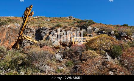 Yellow excavator on rocky hill in nature with clear blue sky in the background, Mani Peninsula, Peloponnese, Greece Stock Photo