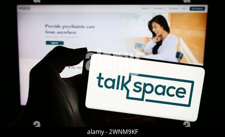 Person holding mobile phone with logo of American online psychotherapy company Talkspace Inc. in front of web page. Focus on phone display. Stock Photo