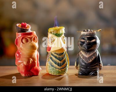 Tiki Drink Cocktails Collection. Set of three tropical tiki cocktails on bar counter. Beautiful tiki cocktails, different decorated with fire flame on bar in night club Stock Photo