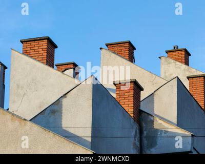 Rising above. Building rooftop brick chimneys against the vast blue skyline. Stock Photo