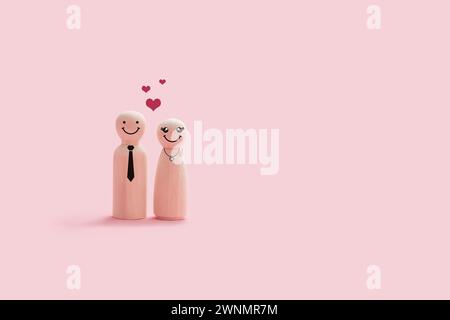 Happy wooden couple figures isolated on a pink background. The couple smiling and stand close together with hearts shape on their head Stock Photo