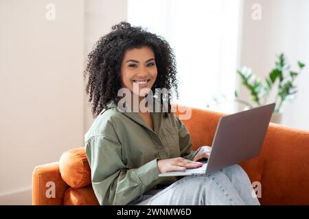 Happy young programmer black woman works on laptop at home Stock Photo
