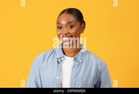 Successful smiling African American woman stands against yellow background Stock Photo