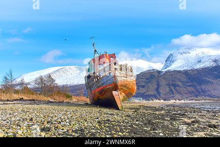 Corpach Fort William Scotland Old Boat of Caol the shipwreck on the rocky beach with Ben Nevis mountain covered with snow Stock Photo