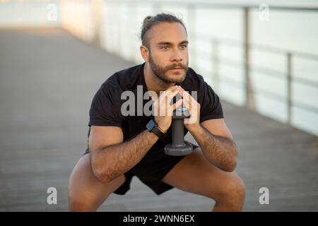 Athlete man performing squats holding dumbbell weights working out outside Stock Photo
