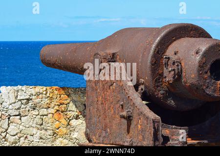 Old Rusty Cannon pressed against the stone wall at El Morro Fortress over looking the deep blue ocean water in Havana Cuba. Stock Photo