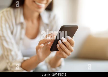 Unrecognizable Woman Using Modern Smartphone While Sitting On Couch At Home Stock Photo