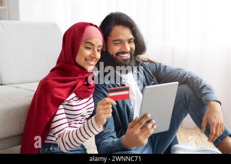 Online Payments. Smiling Muslim Spouses Using Digital Tablet And Credit Card Stock Photo