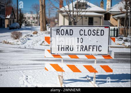 Road closed sign bars traffic from snow covered road in the winter season and winter snow storms. Stock Photo