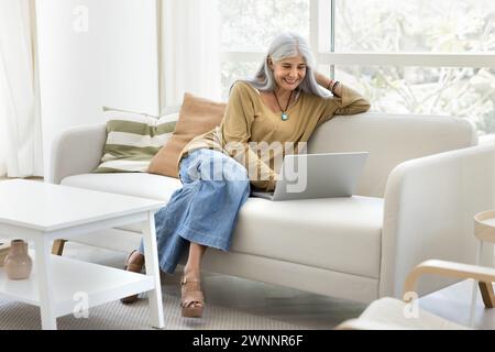 Happy senior elder Latin woman typing on laptop Stock Photo