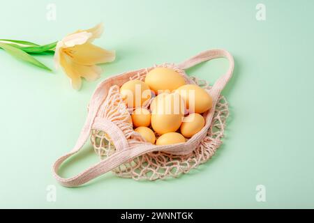 String bag with Easter eggs and yellow tulip on light green background. Top view, flat lay. Stock Photo