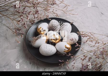 Black plate with Easter eggs and flowers on textured gray background. Top view. Stock Photo