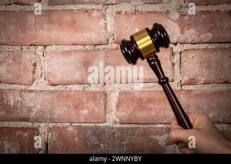 Judge hand holding gavel. Red brick background. Stock Photo