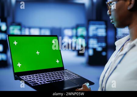 Programmer in server room uses green screen laptop to future proof network from downtimes and unexpected system failures. Tech support with mockup device ensures increased data security Stock Photo