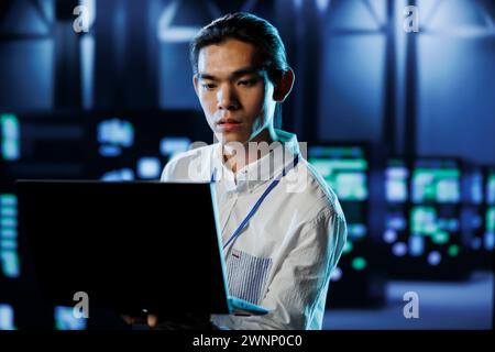 Qualified engineer between server hub rows providing processing resources for businesses worldwide. Certified expert fixing data center mainframes tasked with managing massive databases Stock Photo