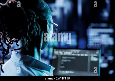 Trained admin running code and programming on laptop, troubleshooting and upgrading high tech facility designed to accommodate multiple rows of fully operational server racks Stock Photo