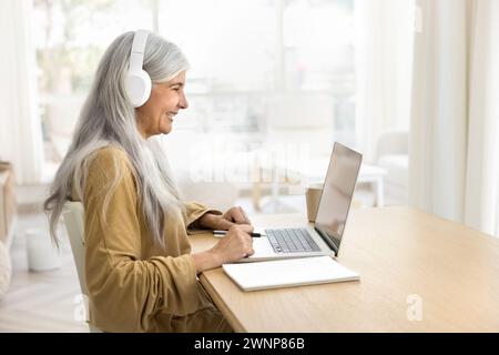 Cheerful retired student woman in big headphones studying on Internet Stock Photo