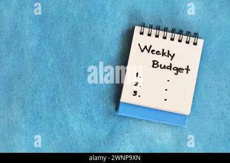 Weekly budgeting concept. White note pad isolated on blue background. Stock Photo