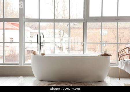 Bathtub with accessories and burning candles near window in room Stock Photo