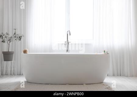 Bathtub with burning candles and spa stones near window in room Stock Photo