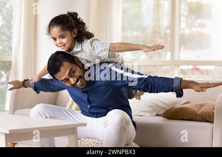 Joyful excited little Indian daughter girl riding dads back Stock Photo