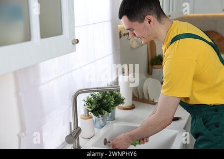 Young plumber wearing uniform repairing sink in kitchen Stock Photo
