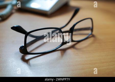 A black eyeglasses and an old landline telephone on wood table, shallow focus. Stock Photo