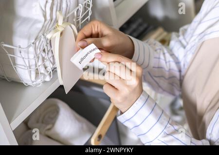 Woman hands organizing cotton pillowcase storage in basket with sticker tag mark at closet shelf Stock Photo