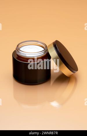 Face cream jar on beige background. Anti-aging balm. Luxury beauty product. Open container with cap. Cosmetic moisturizer. Empty place for text, blank Stock Photo